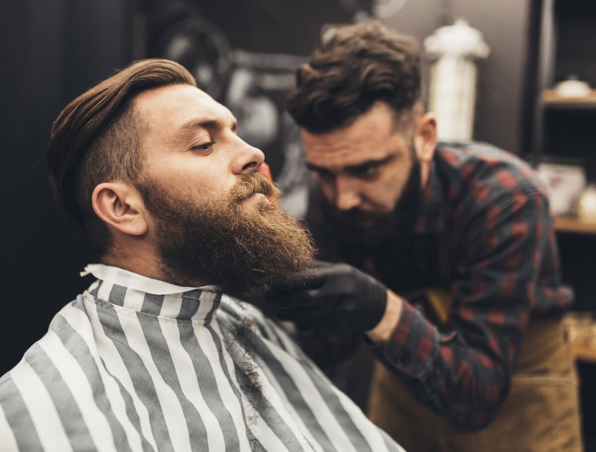 Man with a fresh fade haircut and full beard being groomed by a barber.