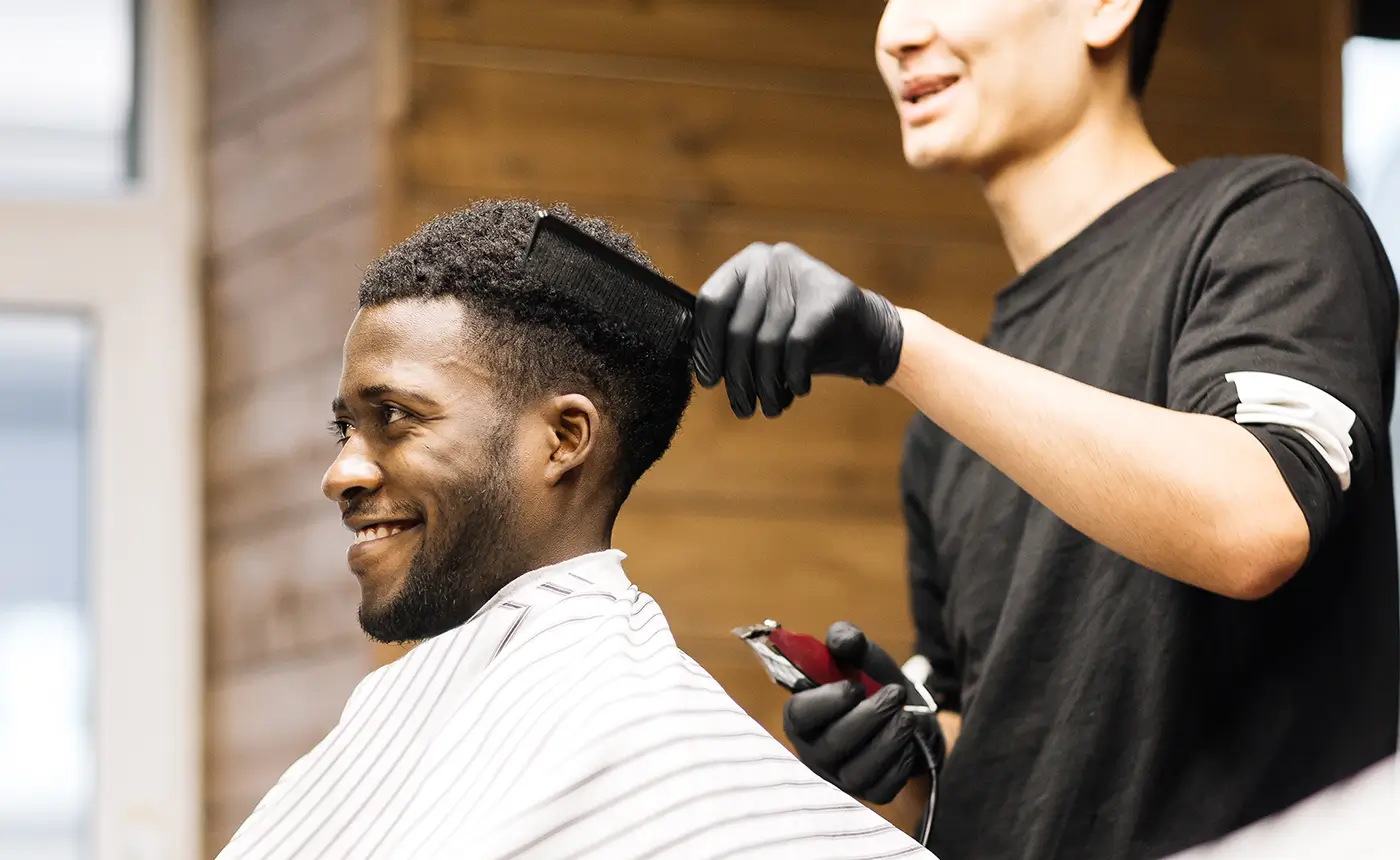 Barber brushing and finishing a client's haircut with clippers in hand